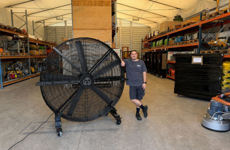 Mobiler ecoBreezer® AirMax mit schwarzen Rotorblättern in einer Lagerhalle neben Geschäftsführer Christopher Schadt